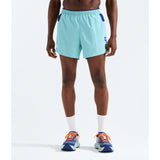 A model from the waist down wearing light blue athletic shorts with dark blue side accents, white crew socks, and blue running shoes with orange laces, set against a plain white studio background. - The North Face Summit Series Pacesetter 5" Run Shorts-Graphic (Men's) - Canal Blue