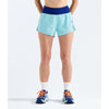A model from the waist down wearing light blue athletic running shorts with a dark blue waistband, white crew socks, and blue running shoes with orange laces, set against a plain white studio background. - The North Face Summit Pacesetter Short-Graphic (Women's) - Canal Blue
