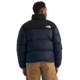 A man viewed from the back wearing a puffer jacket with a black upper section and a dark navy lower section, paired with tan cargo pants against a plain white background. - The North Face 1996 Retro Nuptse Jacket (Men's) - Summit Navy/TNF Black