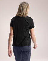 A woman with shoulder-length blonde hair is shown from the back wearing a black short-sleeve scrub top and navy blue scrub pants against a solid light beige background. - Arc'teryx Lana Merino Wool Crew Short-Sleeve T-Shirt (Women's) - Black