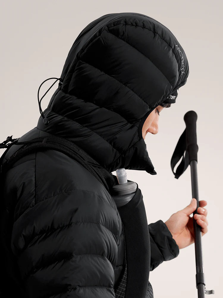 Person wearing a black puffer jacket with a hood, holding ski poles against a light background - Arc'teryx Cerium Hoody (Men's) - Black