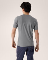 A man viewed from behind wearing a heather gray short-sleeve athletic t-shirt and navy blue pants, standing against a light beige studio background. - Arc'teryx Merino Wool Shirt Short Sleeve (Men's) - Void