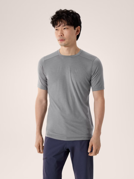 A man wearing a light gray short-sleeve athletic t-shirt and navy blue pants, standing against a solid light beige background. - Arc'teryx Merino Wool Shirt Short Sleeve (Men's) - Void