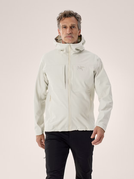 A man wearing a light off-white Arc'teryx hooded jacket and black pants, standing against a solid light beige studio background. - Arc'teryx Gamma MX Hoody (Men's) - Sea Salt
