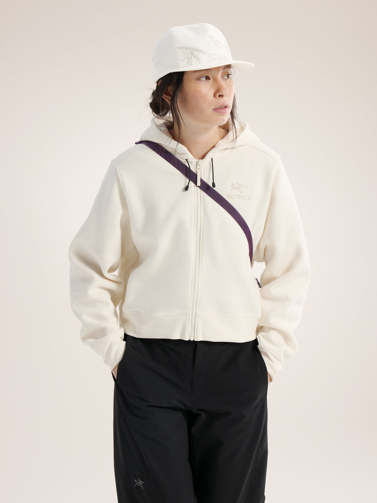 Person wearing a white hoodie with a purple zipper and black pants on a light background - Arc'teryx Mantis 2 Waist Pack - Moondrop