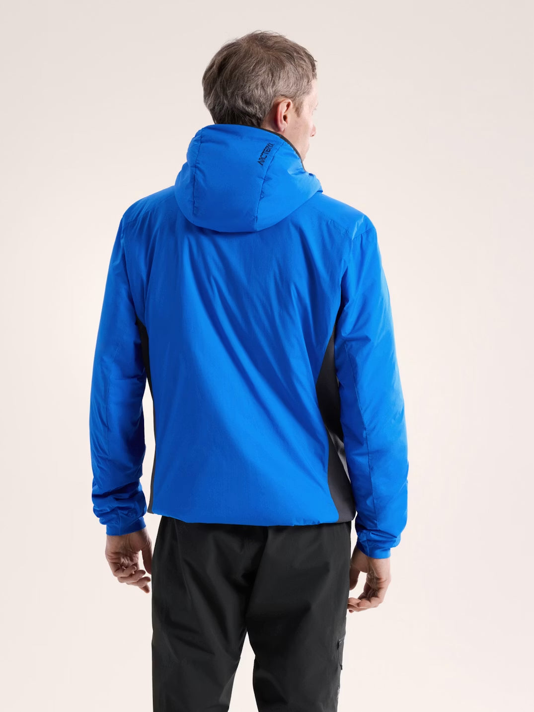 Person wearing a blue jacket with a hood on a beige background - Arc'teryx Atom Hoody (Men's) - Fluidity/Black Sapphire