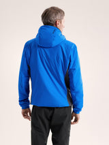 Person wearing a blue jacket with a hood on a beige background - Arc'teryx Atom Hoody (Men's) - Fluidity/Black Sapphire