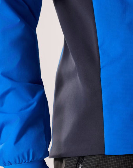 Close-up of a color-blocked jacket with a bright blue sleeve and body panel, a dark charcoal gray center panel, and a small portion of black grid-patterned fabric at the bottom. - Arc'teryx Atom Hoody (Men's) - Fluidity/Black Sapphire