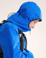 A close-up side profile of a person wearing a bright blue hooded rain jacket with black trim and drawstrings, against a plain light background. - Arc'teryx Atom Hoody (Men's) - Fluidity/Black Sapphire