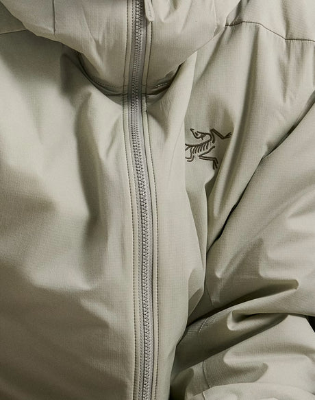 Close-up of a light beige hooded jacket with a central zipper and the Arc'teryx bird logo embroidered on the chest. - Arc'teryx Atom Hoody (Men's) - Habitat