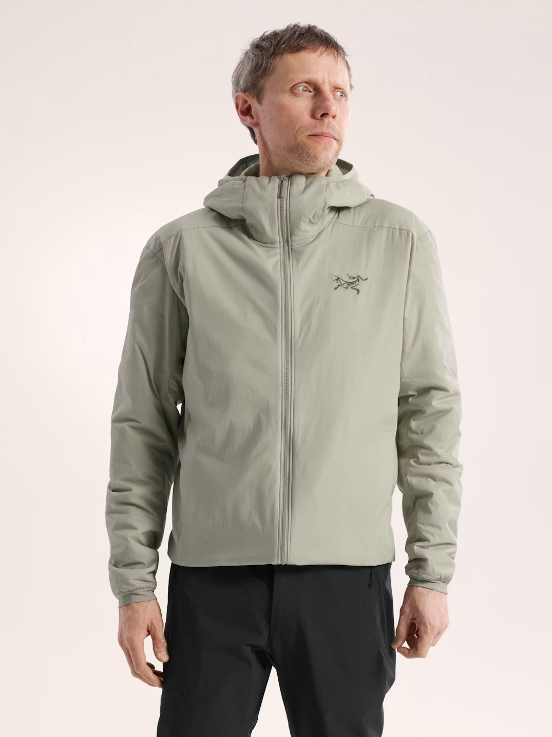 Man wearing a green jacket with a brand logo on a beige background - Arc'teryx Atom Hoody (Men's) - Habitat