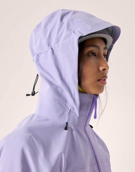 A close-up side profile of a model wearing a light lavender Arc'teryx hooded jacket against a solid light beige background. - Arc'teryx Beta AR GORE-TEX Jacket (Women's) - Mallow