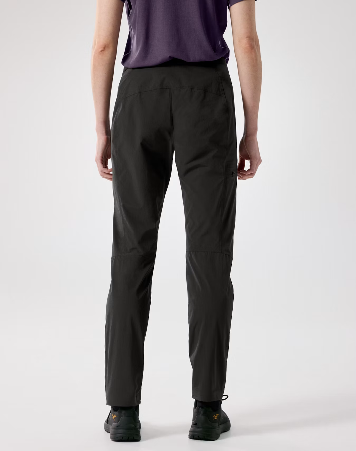 Rear view of a person wearing black tapered pants, a dark purple t-shirt, and black shoes against a light gray studio background. - Arc'teryx Gamma SL Pants (Women's) - Black
