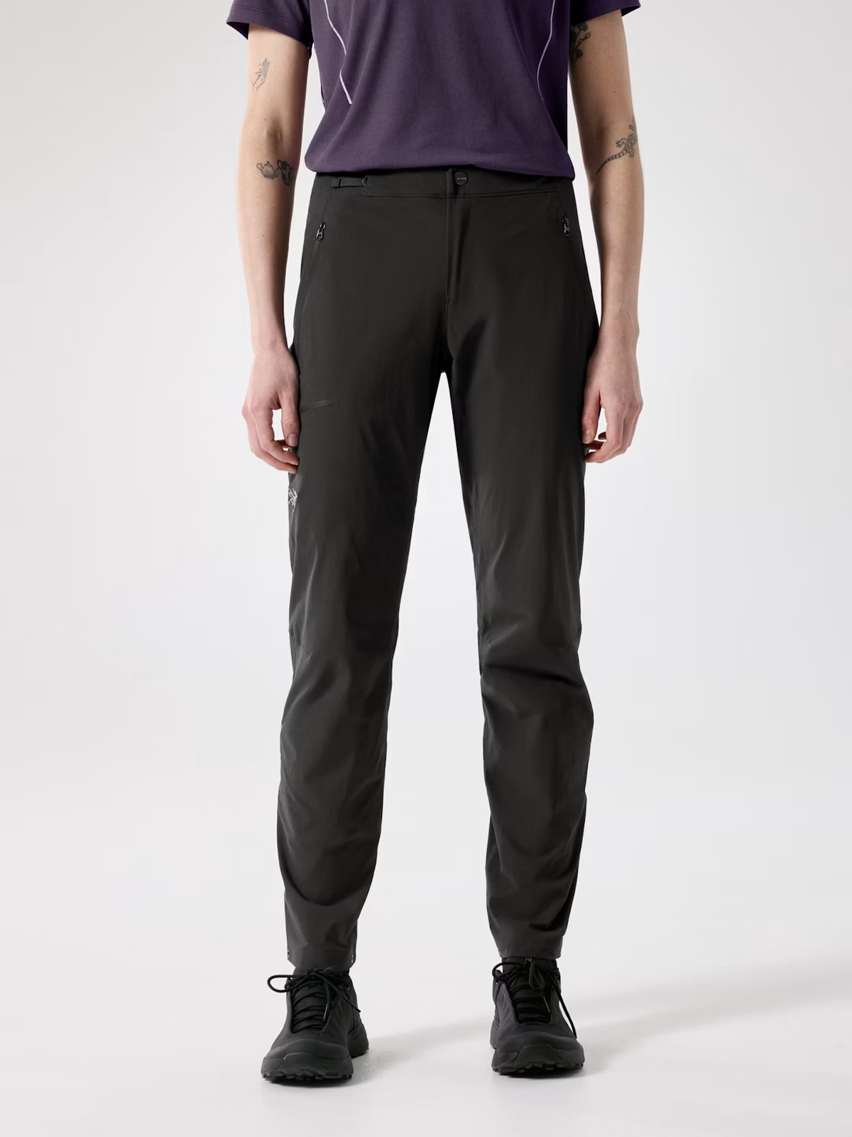 A model from the waist down wearing dark charcoal gray technical pants, a purple t-shirt, and black sneakers, standing against a light gray studio background. - Arc'teryx Gamma SL Pants (Women's) - Black