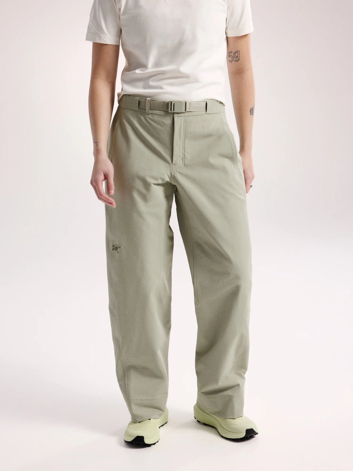 A model wearing light sage green relaxed-fit pants with a matching belt, styled with a white t-shirt and light green sneakers against a plain light background. - Arc'teryx Nia Pants (Women's) - Habitat