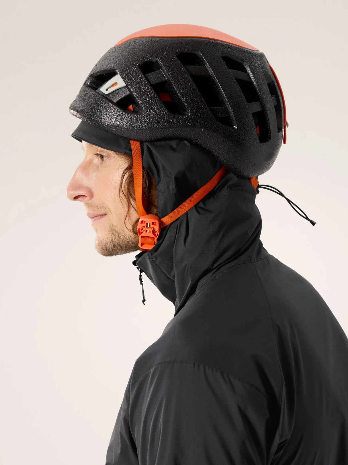 Person wearing a black helmet with orange accents and a black jacket on a light gray background - Arc'teryx Squamish Hoody (Men's) - Black