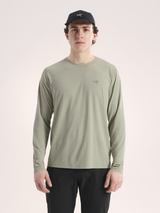 Man wearing a green long-sleeve shirt and black cap on a light pink background - Arc'teryx Cormac Crew Neck Shirt Long Sleeve (Men's) - Habitat