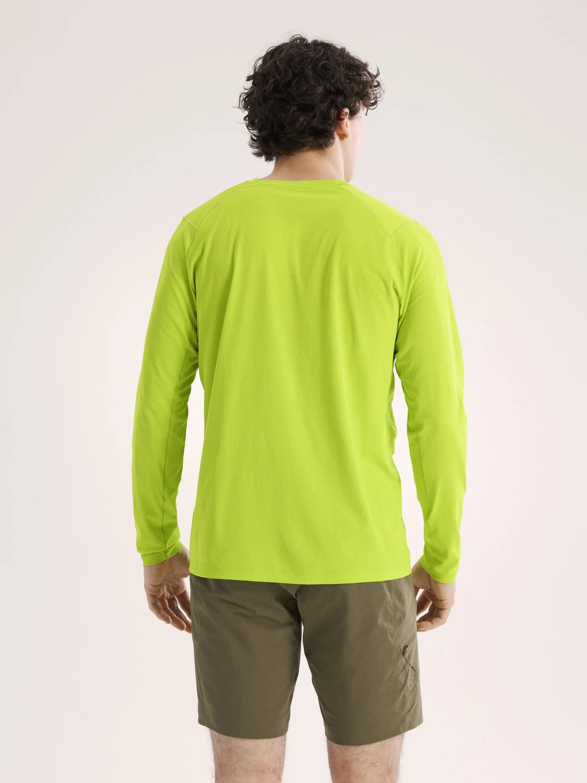 Person wearing a bright green long-sleeve shirt and brown shorts on a light gray background - Arc'teryx Cormac Crew Neck Shirt Long Sleeve (Men's) - Mantis
