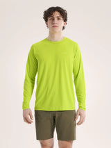 A man wearing a bright lime green long-sleeve crewneck shirt and olive green shorts, standing against a plain light beige studio background. - Arc'teryx Cormac Crew Neck Shirt Long Sleeve (Men's) - Mantis