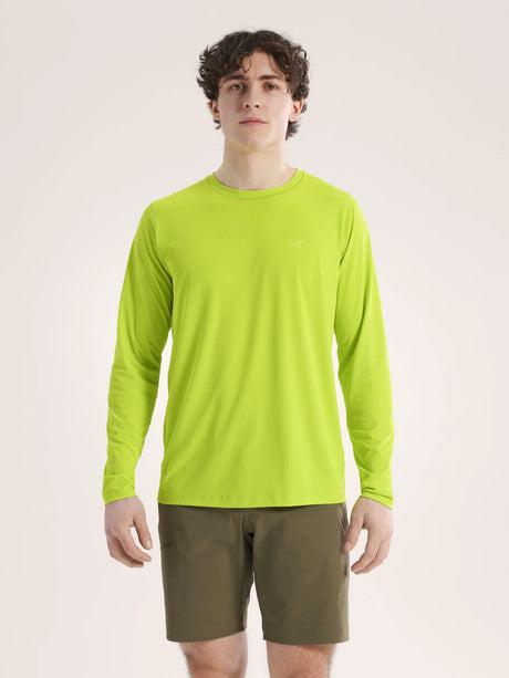 A man wearing a bright lime green long-sleeve crewneck shirt and olive green shorts, standing against a plain light beige studio background. - Arc'teryx Cormac Crew Neck Shirt Long Sleeve (Men's) - Mantis