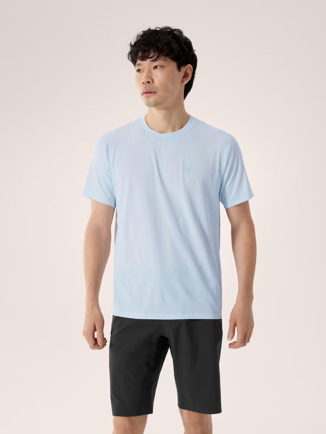 Man wearing a light blue t-shirt and black shorts on a plain background - Arc'teryx Cormac Crew Neck Shirt Short Sleeve (Men's) - Alpine Blue