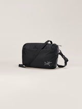 A black nylon crossbody bag with a silver Arc'teryx logo on the front, displayed on a clean, light beige studio background. - Arc'teryx Heliad Crossbody Bag - Black