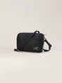 A black nylon crossbody bag with a silver Arc'teryx logo on the front, displayed on a clean, light beige studio background. - Arc'teryx Heliad Crossbody Bag - Black