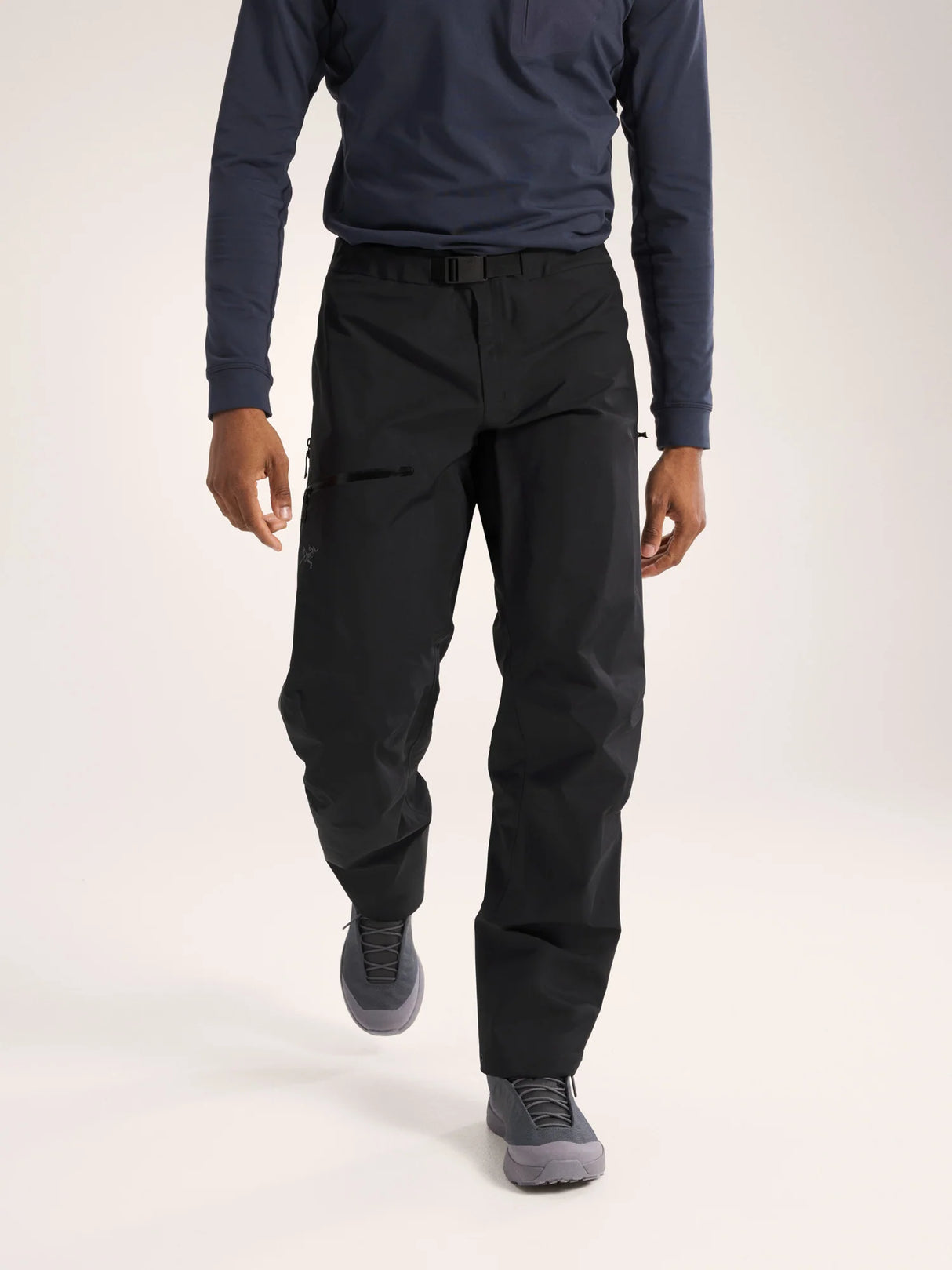 A model wearing black technical cargo pants, a navy long-sleeve shirt, and gray athletic shoes, shown from the chest down against a light gray studio background. - Arc'teryx Beta Pants (Men's) - Black