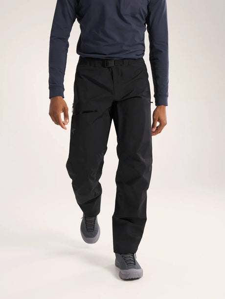 A model wearing black technical cargo pants, a navy long-sleeve shirt, and gray athletic shoes, shown from the chest down against a light gray studio background. - Arc'teryx Beta Pants (Men's) - Black