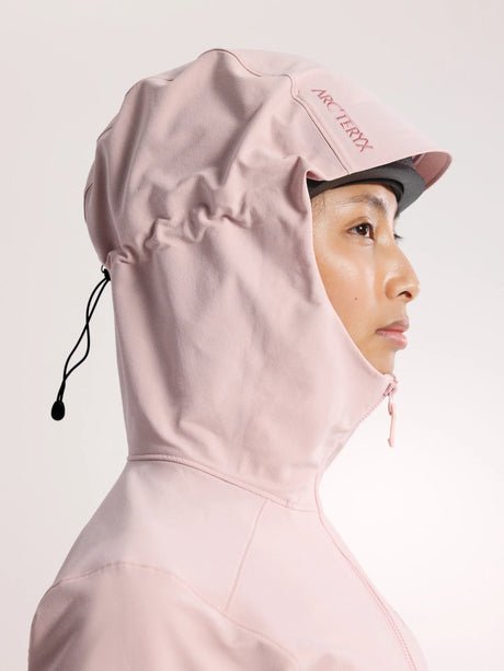 A close-up side profile of a person wearing a light pink Arc'teryx hooded jacket against a clean, light off-white background. - Arc'teryx Gamma Hoody (Women's) - Alpine Rose