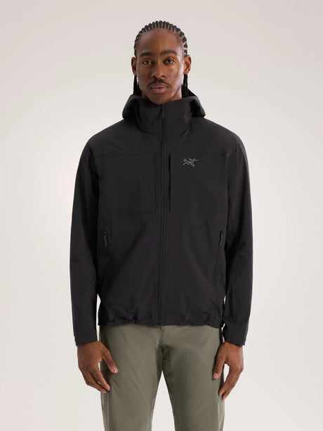 A man wearing a black Arc'teryx hooded jacket and olive green pants, standing against a light gray studio background. - Arc'teryx Gamma Lightweight Hoody (Men's) - Black