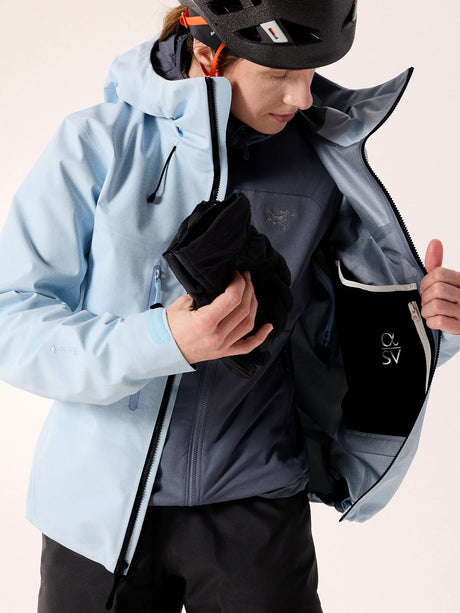 Person wearing a light blue jacket with a black backpack, on a plain background - Arc'teryx Alpha SV Jacket (Women's) - Alpine Blue/Black