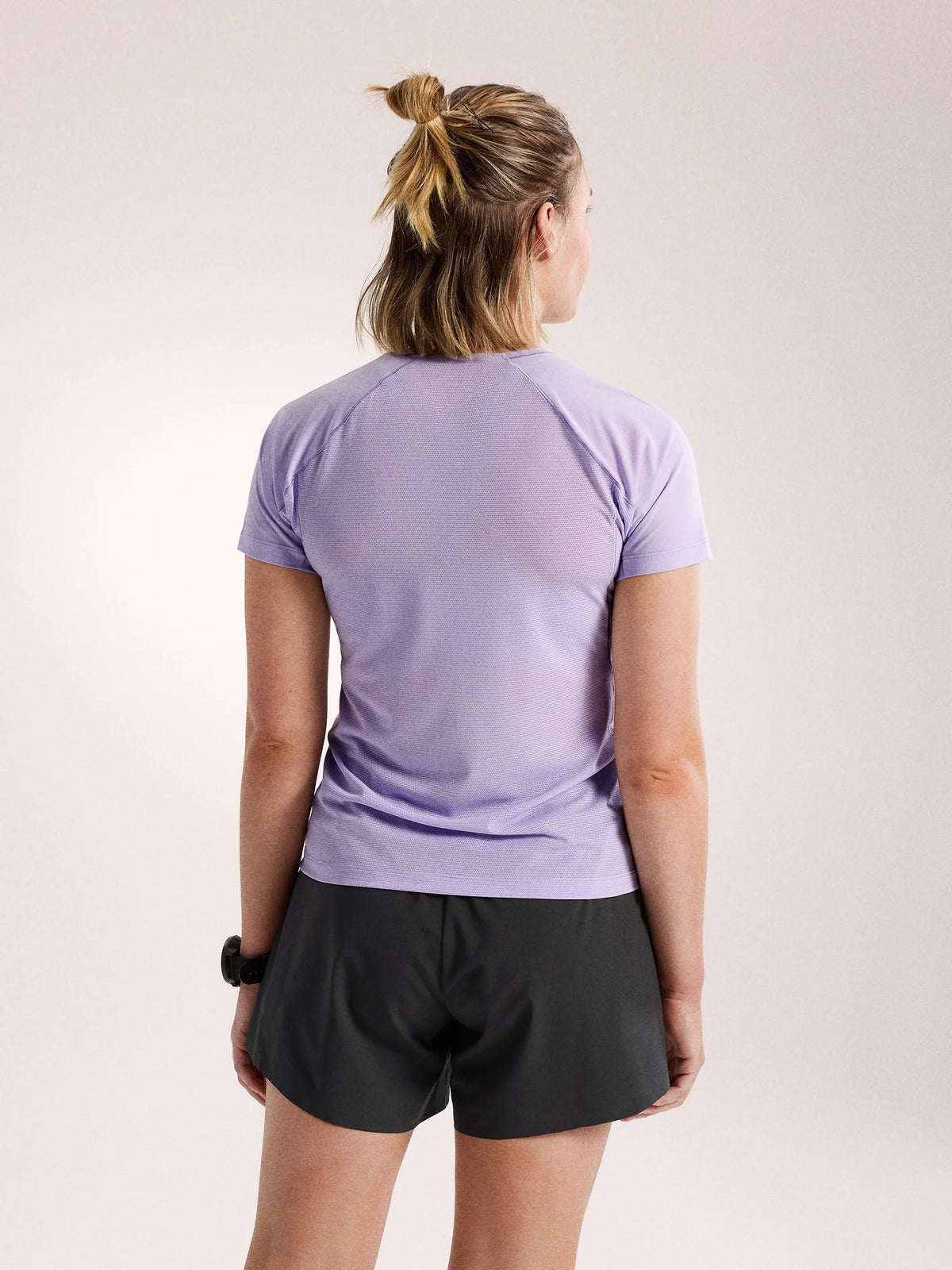 A woman shown from behind wearing a light purple short-sleeve athletic t-shirt and black athletic shorts against a plain light background. - Arc'teryx Norvan Crew Short Sleeve (Women's) - Mallow