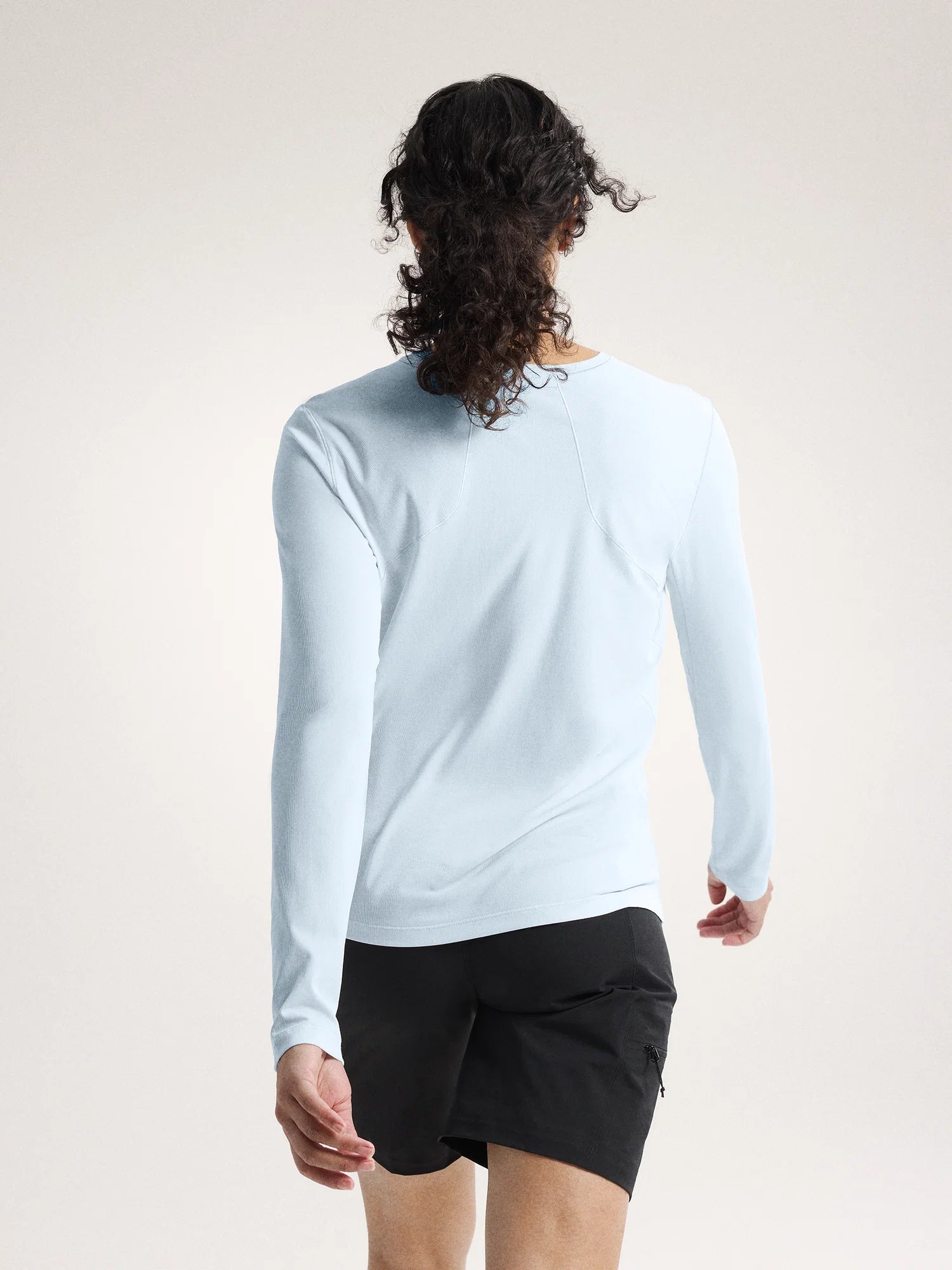 Person wearing a light blue long-sleeve shirt and black shorts on a white background - Arc'teryx Sunna Crew Shirt Long Sleeve (Women's) - Alpine Blue