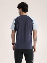 A man viewed from the back wearing a short-sleeve athletic shirt with a dark navy body and light blue shoulder panels, paired with black athletic pants, against a plain light beige studio background. - Arc'teryx Norvan Downword Logo Shirt Short Sleeve (Men's) - Alpine Blue/Dark Stratus