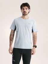 Man wearing a light blue athletic shirt with black sleeves and black pants on a beige background - Arc'teryx Norvan Downword Logo Shirt Short Sleeve (Men's) - Alpine Blue/Dark Stratus