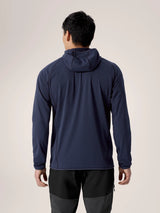 A man viewed from the back wearing a navy blue hooded long-sleeve athletic top and dark gray pants, set against a plain light beige studio background. - Arc'teryx Delta Hoody (Men's) - Black Sapphire