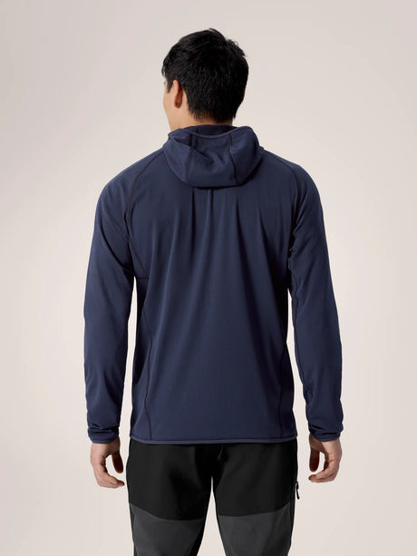 A man viewed from the back wearing a navy blue hooded long-sleeve athletic top and dark gray pants, set against a plain light beige studio background. - Arc'teryx Delta Hoody (Men's) - Black Sapphire