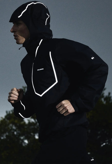 Person wearing a black jacket with reflective white accents running outdoors. - Salomon Bonatti Pro Jacket (Men's) - Deep Black