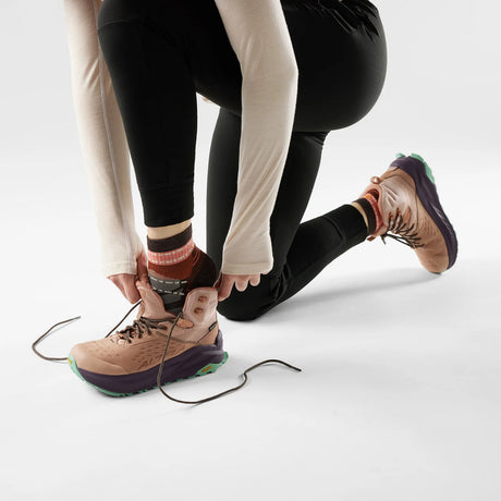 Person adjusting the laces of a brown shoe on a white background - Smartwool Hike Margarita Light Cushion Ankle Socks (Women's) - Chestnut