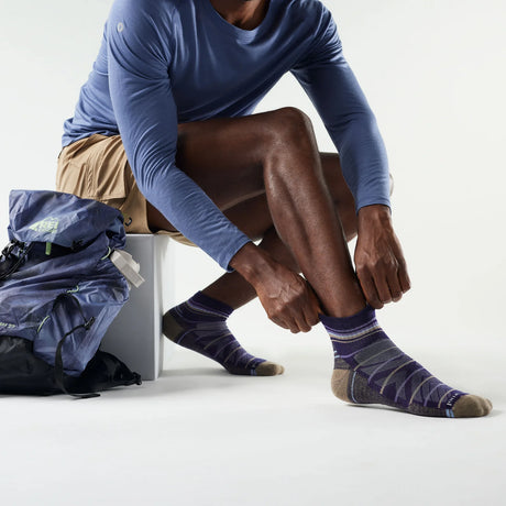 Person wearing blue long-sleeve shirt and patterned socks, sitting with a backpack on a white background - Smartwool Hike Pattern Light Cushion Ankle Socks (Unisex) - Nightfall Blue