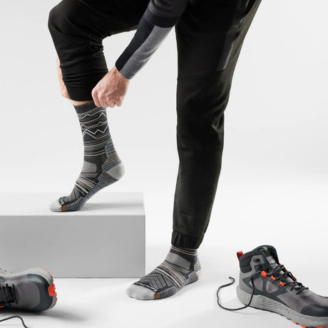 Person wearing black pants and gray patterned socks with hiking shoes on a light gray background - Smartwool Hike Mountain Range Light Cushion Crew Socks (Unisex) - Charcoal/Light Grey