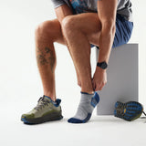 Person wearing gray and blue athletic shoes and socks, sitting on a white surface. - Smartwool Hike Targeted Cushion Low Ankle Socks (Unisex) - Light Grey