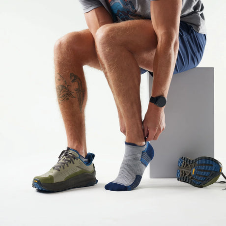 Person wearing gray and blue athletic shoes and socks, sitting on a white surface. - Smartwool Hike Targeted Cushion Low Ankle Socks (Unisex) - Light Grey