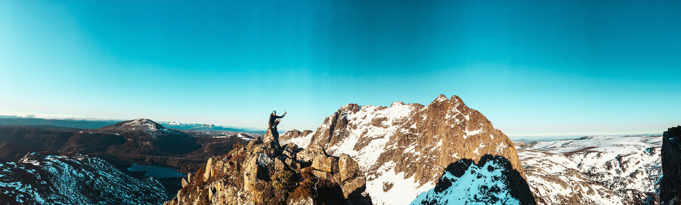 Hanny Allston guide on a find your feet trail running tour sitting on a rocky mountain peak with a scenic view of mountains and a lake.