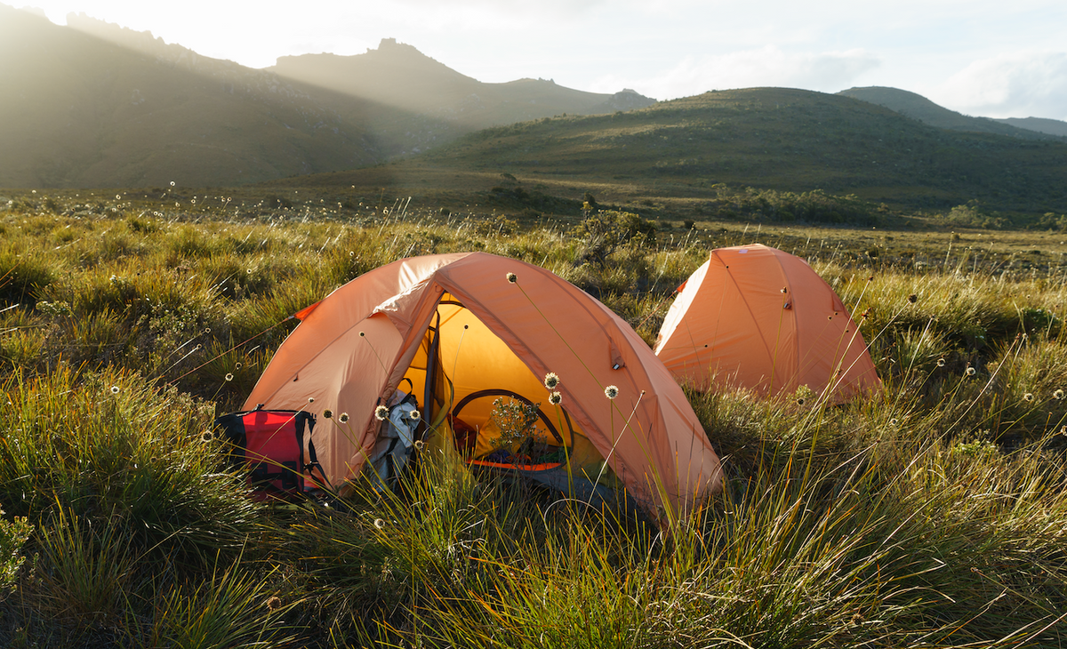 Two orange ONE PLANET goondie tents in a grassy field with mountains in the background