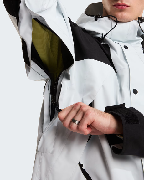 Close-up of a person wearing a color-blocked ski jacket in white, black, and olive green, showing the inner lining and a zippered pocket. - The North Face GORE-TEX Mountain Jacket (Men's) - Pearl Stone/TNF Black
