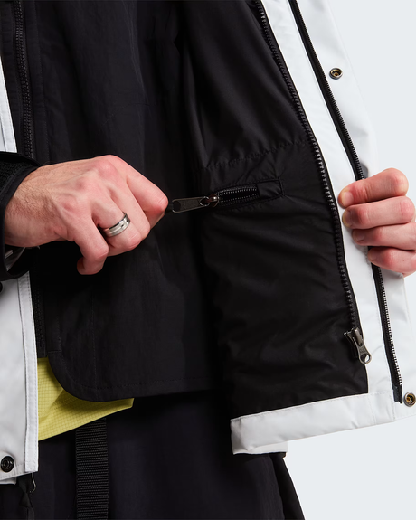 Close-up of a person wearing a black and white jacket, showing hands opening a zippered pocket on the black side panel. - The North Face GORE-TEX Mountain Jacket (Men's) - Pearl Stone/TNF Black