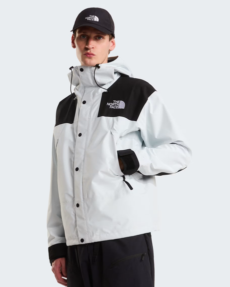 A male model wearing a light gray and black The North Face jacket, a black baseball cap, and black pants, photographed against a solid light gray background. - The North Face GORE-TEX Mountain Jacket (Men's) - Pearl Stone/TNF Black