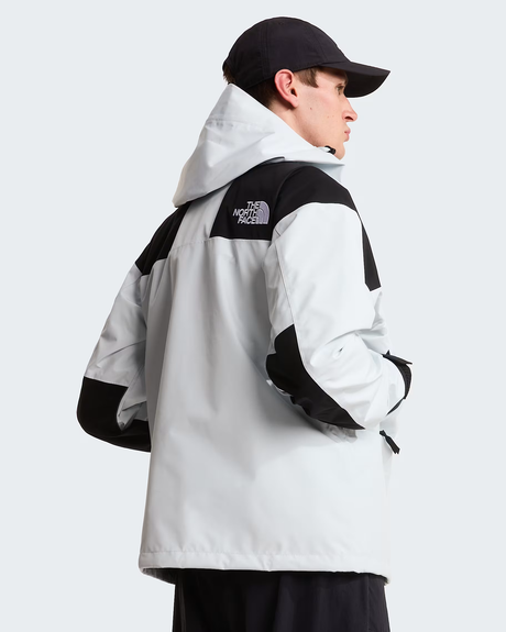 A man wearing a light gray and black color-blocked hooded jacket by The North Face, shown from a side-back angle against a light gray studio background. - The North Face GORE-TEX Mountain Jacket (Men's) - Pearl Stone/TNF Black